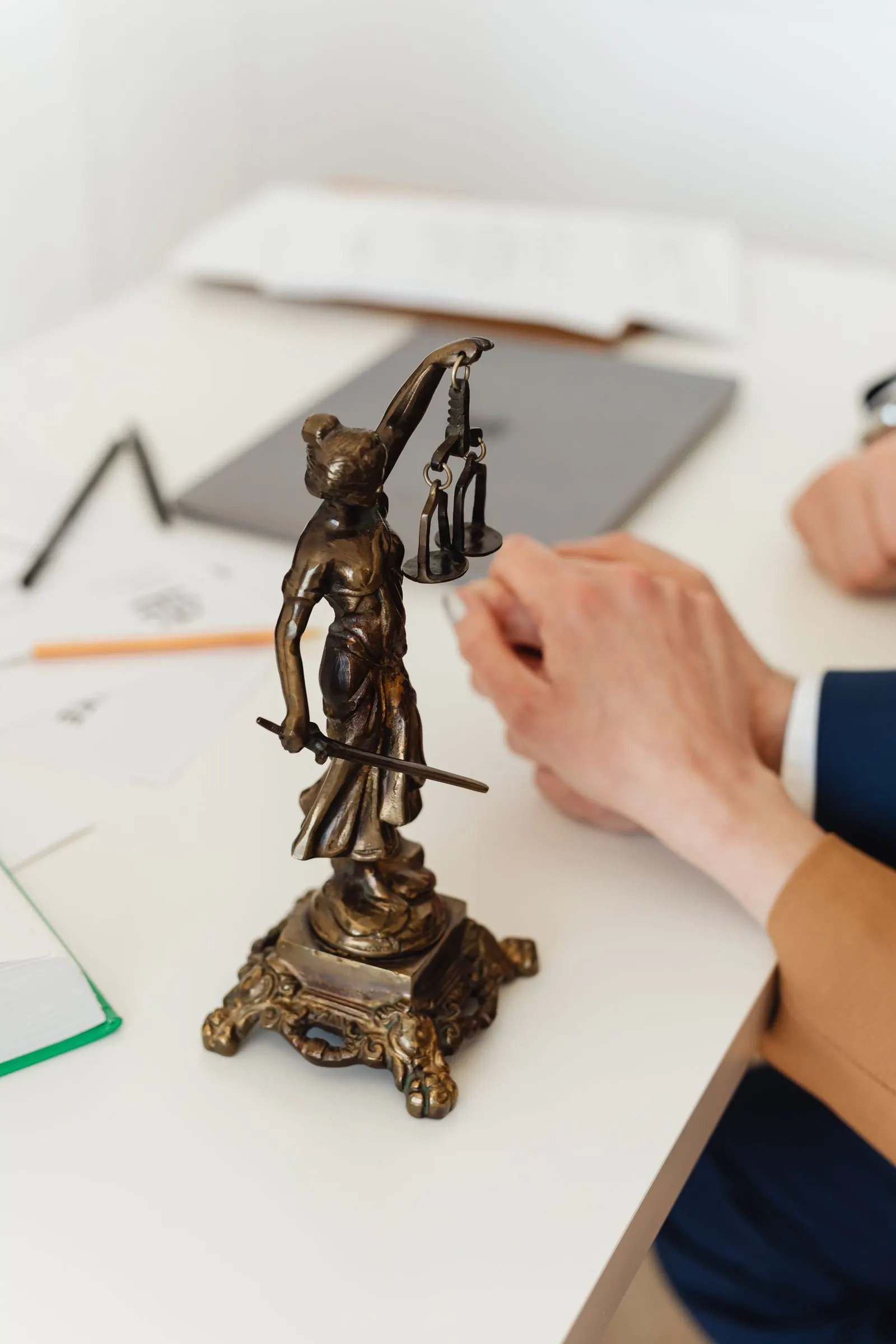 Lady Justice statuette on a lawyer's desk, with a hand resting on a client's hand